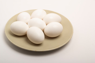 Seven white raw eggs lie on a gray plate on a white background