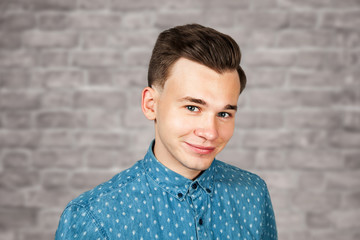 smiling portrait white young guy model dressed in blue shirt looking at the camera on brick wall background