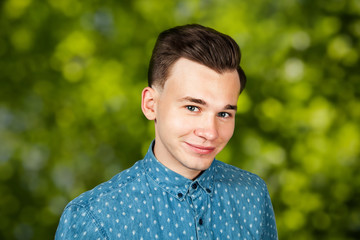 smiling portrait white young guy model dressed in blue shirt looking at the camera on green bokeh background