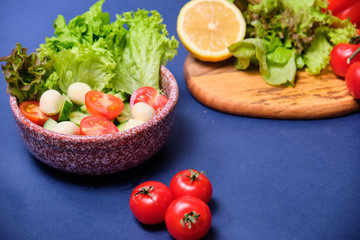 fresh vegetables and a bowl of salad with mozzarella on a blue background.  Caprese salad . Lettuce, cherry tomatoes, mozzarella, 