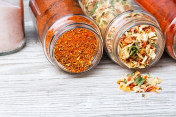 Słoje z przyprawami leżące na drewnianym blacie. Przyprawy i suszone warzywa wysypujące się ze słoika.  Liofilizowane warzywa.