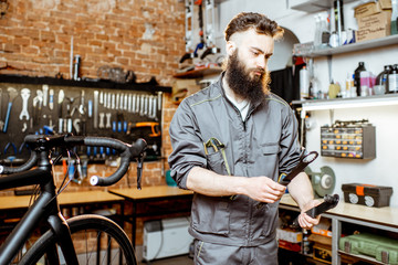Fototapeta na wymiar Handsome bearded repairman in workwear serving a sports bike at the bicycle workshop