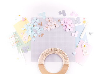 Flat lay, top view craft table desk. Workspace with mat for cutting, scissors, cardstock, paper, pencils on white background. Make floral wreath decor.