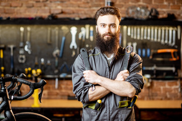 Portrait of a handsome bearded repairman in workwear standing with wrenches at the bicycle workshop