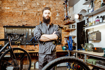 Portrait of a handsome bearded repairman in workwear standing with wrenches at the bicycle workshop