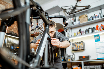 Handsome bearded repairman in workwear serving a sports bike at the bicycle workshop