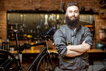Fototapeta na wymiar Portrait of a handsome bearded repairman in workwear at the bicycle workshop