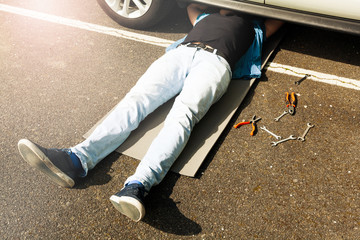 Man lying under auto underbody doing repair work - obrazy, fototapety, plakaty