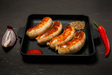 square pan with four sausages, ketchup, caraway, chili, and onion