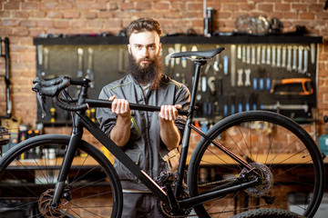 Portrait of a handsome cheerful repairman in workwear holding sports bicycle at the workshop
