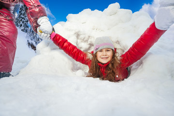 Friends are pulling smiling girl from snow tunnel