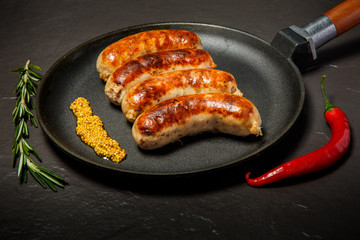 top view fried sausages on round black pan with granular mustard