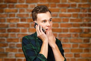 portrait of scared White young guy writes a message on the mobile phone and smiles. Man on brick wall background