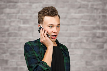 portrait of scared White young guy writes a message on the mobile phone and smiles. Man on brick wall background