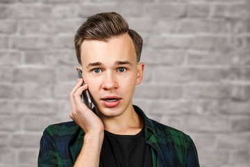 portrait of scared White young guy writes a message on the mobile phone and smiles. Man on brick wall background