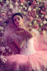 Silence is gold. Top view of beautiful young woman in pink ballet tutu surrounded by flowers. Spring mood and tenderness in coral light. Art photo. Concept of spring, blossom and nature's awakening.