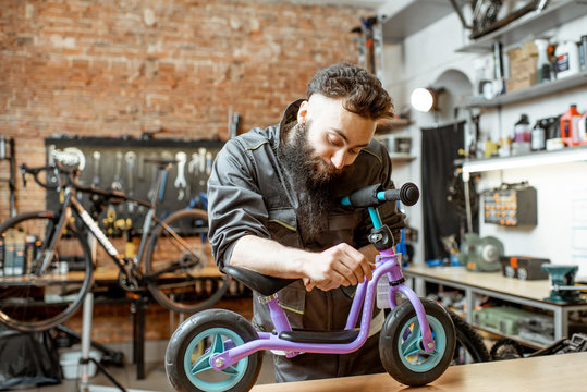 Cheerful repairman in workwear with child bicycle at the workshop of the bicycle store