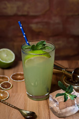 summer alcoholic cocktail mojito green with lime and mint in a glass beaker with ice, mojito cocktail is on a wooden table with a brick wall and bar utensils