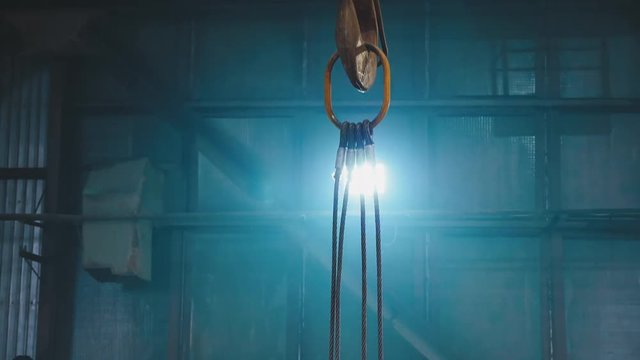 A big industrial hook lifting up, on the blue background through the light from the lamp. A construction plant.