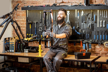 Fototapeta na wymiar Portrait of a handsome repairman in workwear sitting with bicycle fork on the table in the bicycle workshop