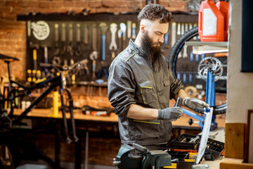 Handsome bearded repairman in workwear working in the beautiful bicycle workshop