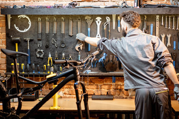 Repairman taking wrenches from the wall with different tools for bicycle repairing indoors