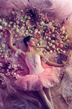 Beauty of sadness. Top view of beautiful young woman in pink ballet tutu surrounded by flowers. Spring mood and tenderness in coral light. Art photo. Concept of spring, blossom and nature's awakening.