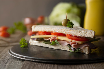 Homemade club sandwich. Toasted white bread triangles with ham, cheese fresh vegetables. Wooden table.