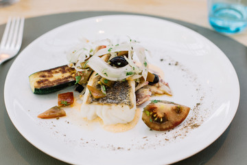 Plated fish with heirloom tomatoes, zucchini, onions and fresh herbs at a restaurant 