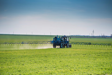 Fototapeta premium Blue tractor with spraying device in green field