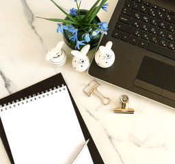Easter concept. Flat lay office table, workspace with laptop, Easter bunny, bouquet blue spring flowers, notebook on marble background.