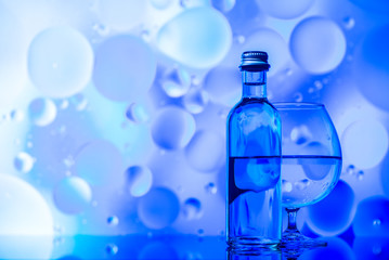 transparent glass and bottle with water and oily drops on azure background 
