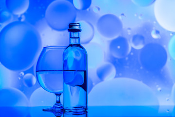 transparent glass and bottle with water and oily drops on azure background 