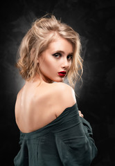 Naklejka premium Beautiful young braless slim blonde girl with disheveled hair and aggressive makeup, wearing an unbuttoned shirt and jeans emotionally posing on a gray background. Commercial design
