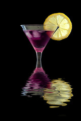 Fresh Purple rain cocktail in a martini glass with ice, garnished with lemon slice on a black textured surface, reflected in water
