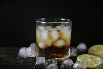 Whiskey with ice in a glass on a black wooden old background with ice and lemon