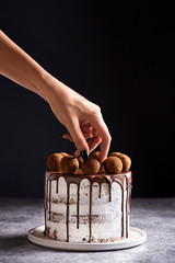 Chocolate cake. Woman hand decorating cocoa balls on top of the round cake with chocolate coating.