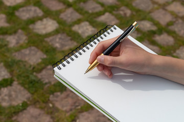 Boy's hand with a pencil over an open notepad in the park.