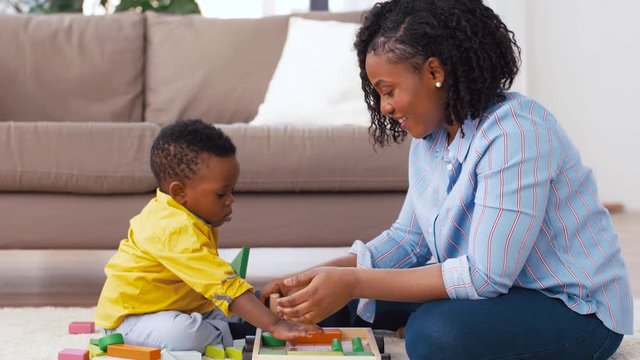 childhood, kids and people concept - happy african american mother and her baby son playing together with wooden toy blocks kit on floor at home