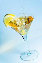 Olive splashing on a glass of martini with a slice of lemon