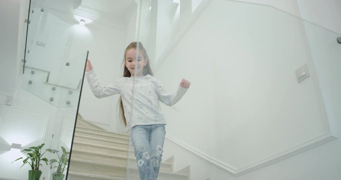 A small girl six years old in the morning in a modern house design stairs she coming down to the first floor.