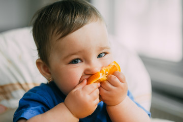 a little girl in a blue t-shirt and a blue plate sitting in a child's chair eating an orange