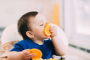 a little girl in a blue t-shirt and a blue plate sitting in a child's chair eating an orange