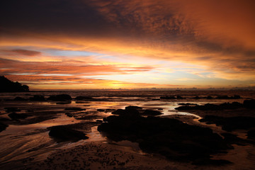 Fototapeta na wymiar Sky with deep hanging storm clouds and wet sludge during low tide swathed in yellow and red bright light during sunset on tropical island Ko Lanta, Thailand