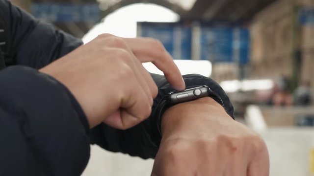 Close - up shot of male's hand uses of wearable smart watch while standing at railway station
