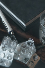 suicide: empty blisters next to a glass of water, notepad and pen, toning. short focus, haze, blur