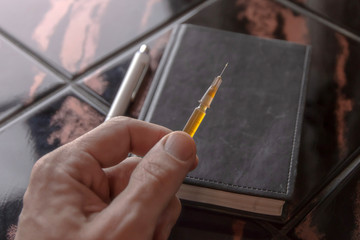 syringe in a person's hand, on a notepad background, short focus, toning