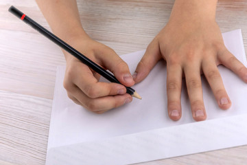 boy signs blank envelopes lying on a wooden table, close-up, low contrast, haze effect