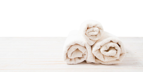 Rolled white towels on white wooden table isolated on white background. Copy space and top view. Bathroom objects for shower body treatment. Selective focus. Banner