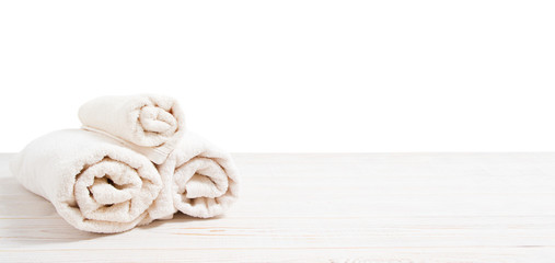 Rolled white towels on white wooden table isolated on white background. Copy space and top view. Bathroom objects for shower body treatment. Selective focus. Banner